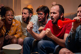 Excited group of male fan screaming and watching match and celebrating goal of favorite team with friends in evening at home. Soccer supporters having fun together sitting on a sofa in the living room