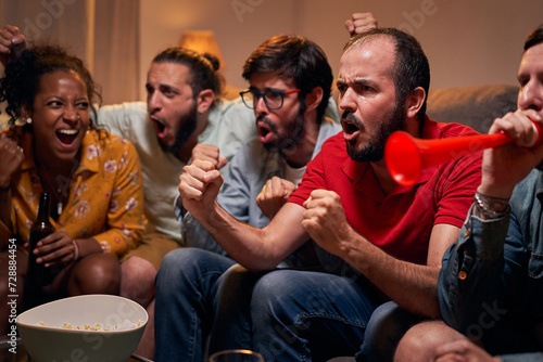 Excited group of male fan screaming and watching match and celebrating goal of favorite team with friends in evening at home. Soccer supporters having fun together sitting on a sofa in the living room © CarlosBarquero
