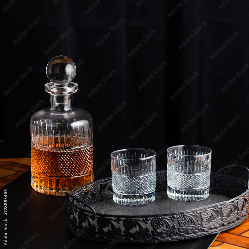 Whiskey bottle and goblets on a wooden table and black tray Whiskey bottle and goblets on a wooden table and black tray