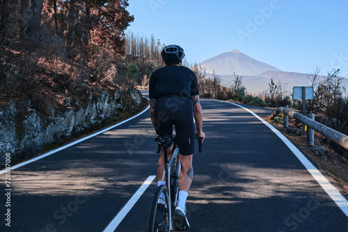 Male cyclist pedaling on road with view on mountain Teide volcano Tenerife Canary Islands Spain. Sportsman training hard on bicycle outdoors.Sport motivation.Cycling training outdoors.Hipster cyclist.