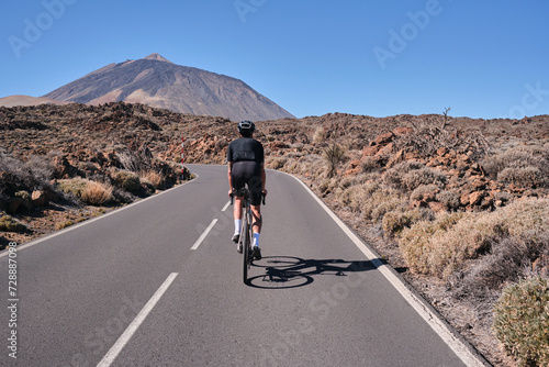 Male cyclist pedaling on road with view on mountain Teide volcano,Tenerife,Canary Islands,Spain. Sportsman training hard on bicycle outdoors.Sport motivation.Cycling training outdoors.Hipster cyclist.