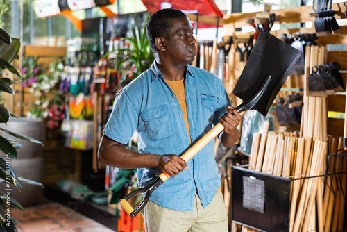 Focused adult african american man choosing shovel to working in his garden at gardening tools store.. photo