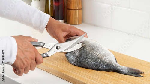 Closeup of man using poultry shears on a fish. (ID: 728890697)