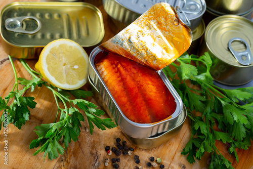 Canned sea fish, mackerel fillets in tomato served with herbs and lemon on wooden table photo