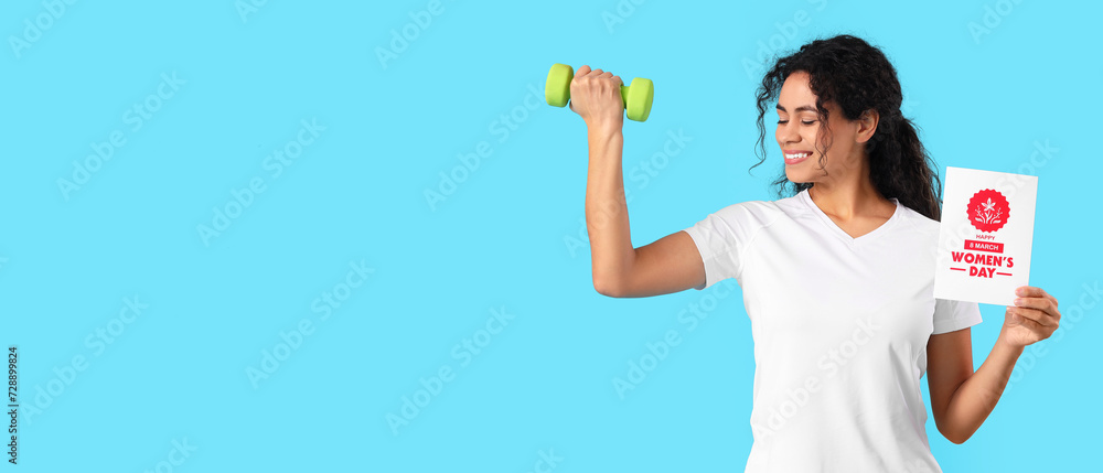 Young African-American woman with greeting card and dumbbell on blue background with space for text. International Women's Day celebration Young African-American woman with greeting card and dumbbell on blue background with space for text. International Women's Day celebration