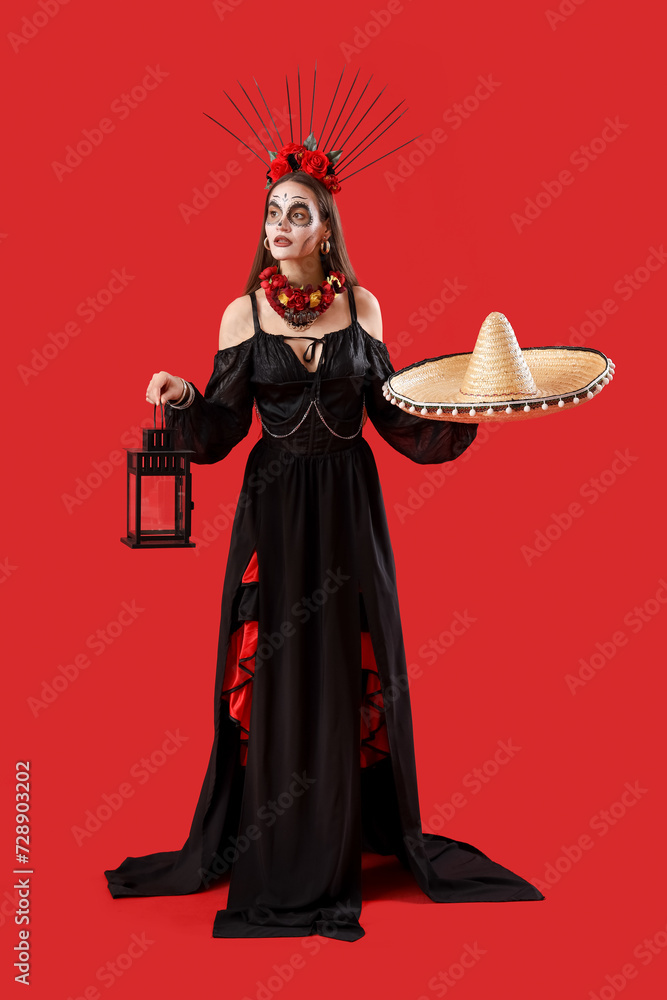 Young woman with painted skull on her face, sombrero and lantern against red background. Celebration of Mexico's Day of the Dead (El Dia de Muertos)