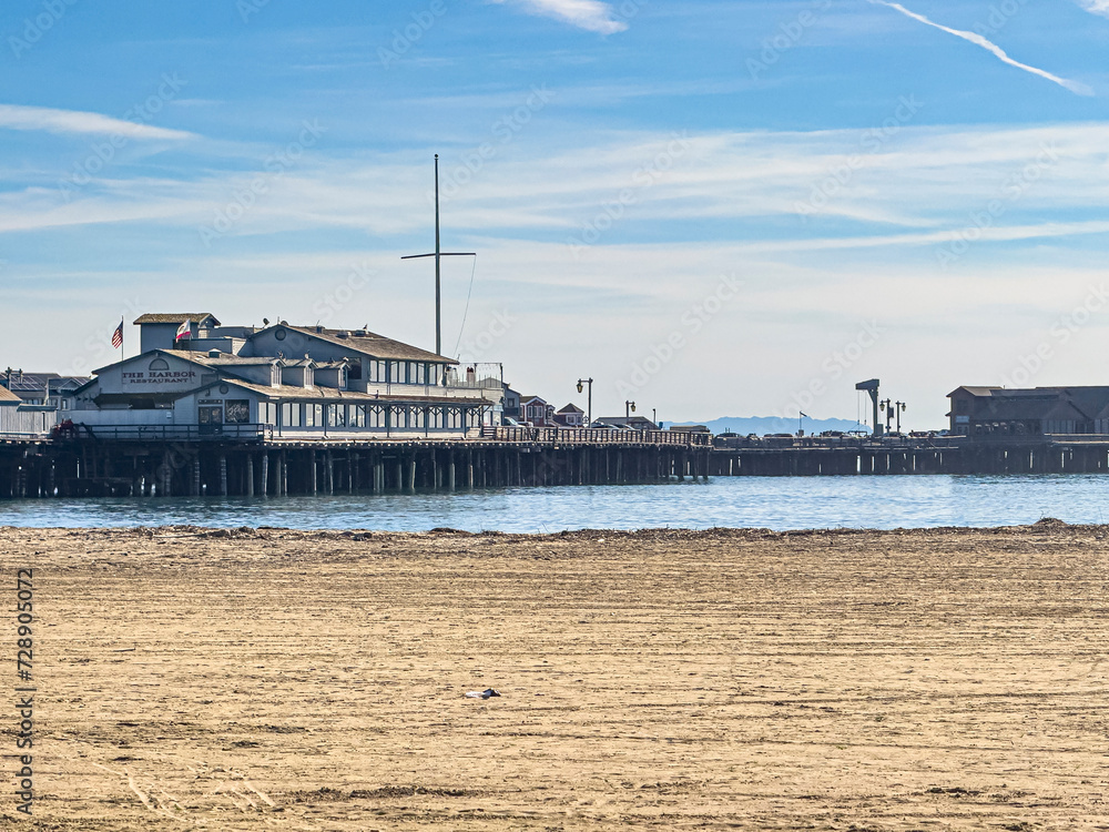 Santa Barbara, CA, USA - January 28, 2024: Harbor Restaurant on Stearns wharf behind sandy West Beach under blue cloudscape
