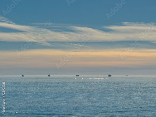 Santa Barbara, CA, USA - January 28, 2024: Five offshore oil rigs on horizon in Pacific Ocean under morning blue sky cover with orange sunlight. Swimmer in front  © Klodien