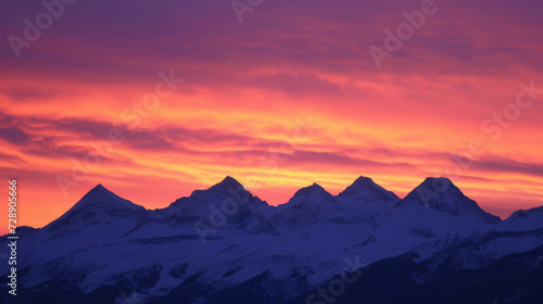 The sharp peaks of a mountain range are silhouetted against a blazing orange and pink sunrise sky.