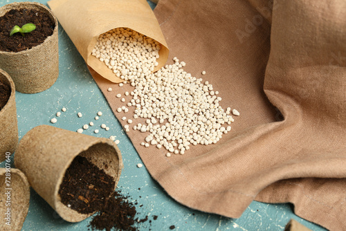 Bag with granular fertilizer and peat pots on blue grunge background photo