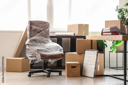 Interior of light office with chair wrapped in stretch film and cardboard boxes on moving day © Pixel-Shot