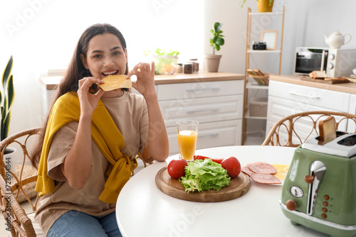 Young beautiful happy woman eating tasty sandwich in kitchen