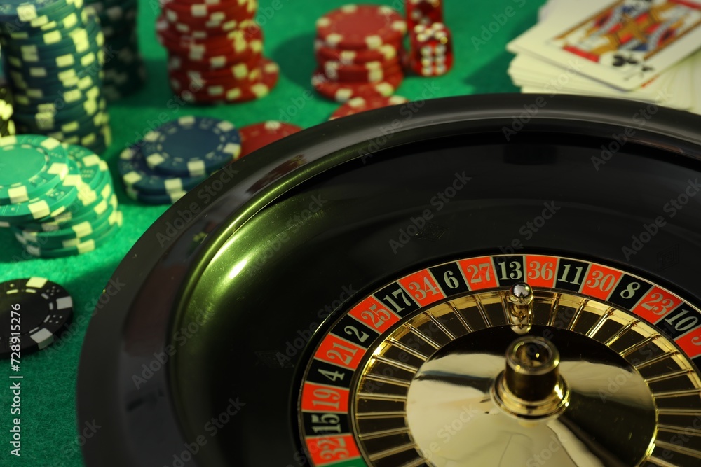 Roulette wheel with ball, playing cards and chips on green table, closeup. Casino game Roulette wheel with ball, playing cards and chips on green table, closeup. Casino game