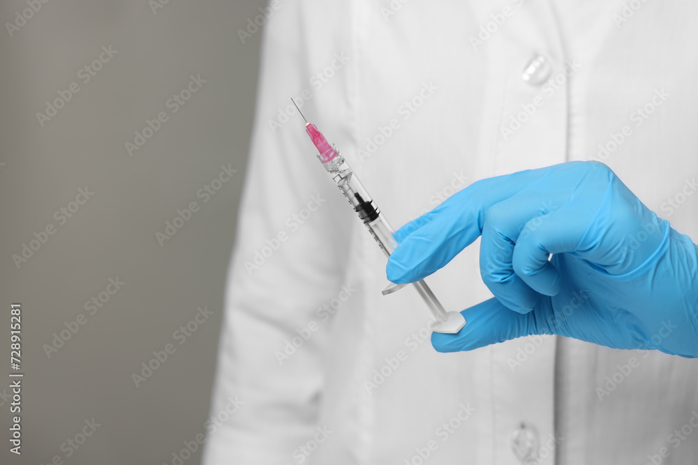 Doctor holding syringe on grey background, closeup. Space for text Doctor holding syringe on grey background, closeup. Space for text