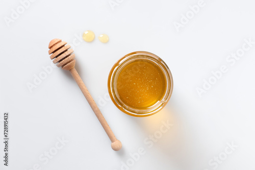 Tasty honey in glass jar and dipper on white background, top view