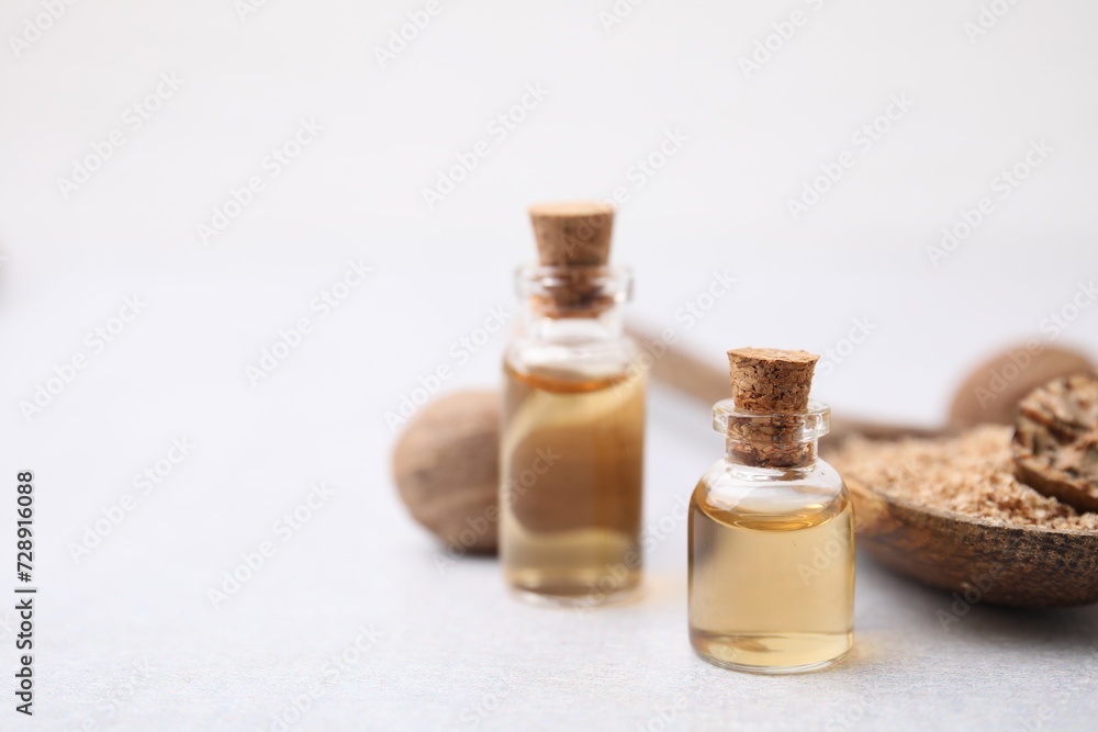 Nutmeg essential oil and spoon with ground nuts on light table, closeup. Space for text