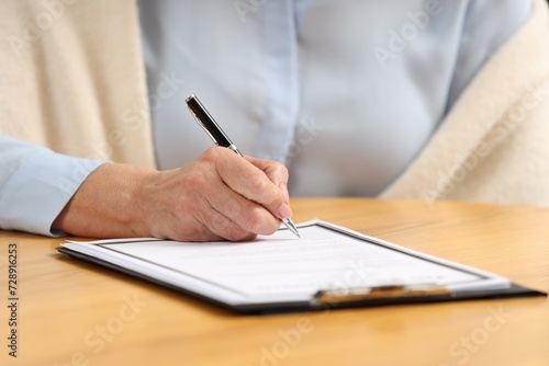 Senior woman signing Last Will and Testament at wooden table, closeup