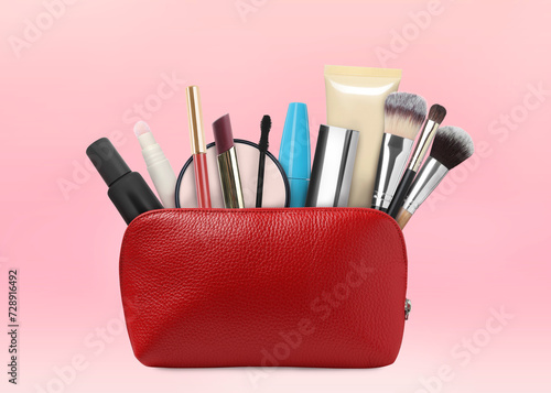 Cosmetic bag filled with makeup products on pink background
