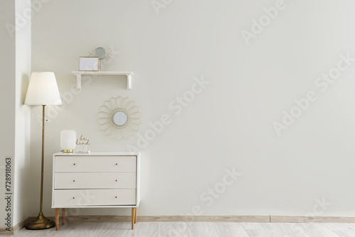 Chest of drawers with lamp, mirror and decor near white wall © Pixel-Shot