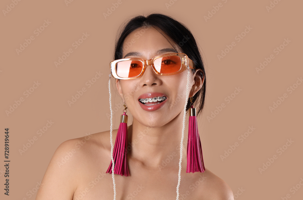 Young Asian woman with sunglasses and earrings on beige background Young Asian woman with sunglasses and earrings on beige background