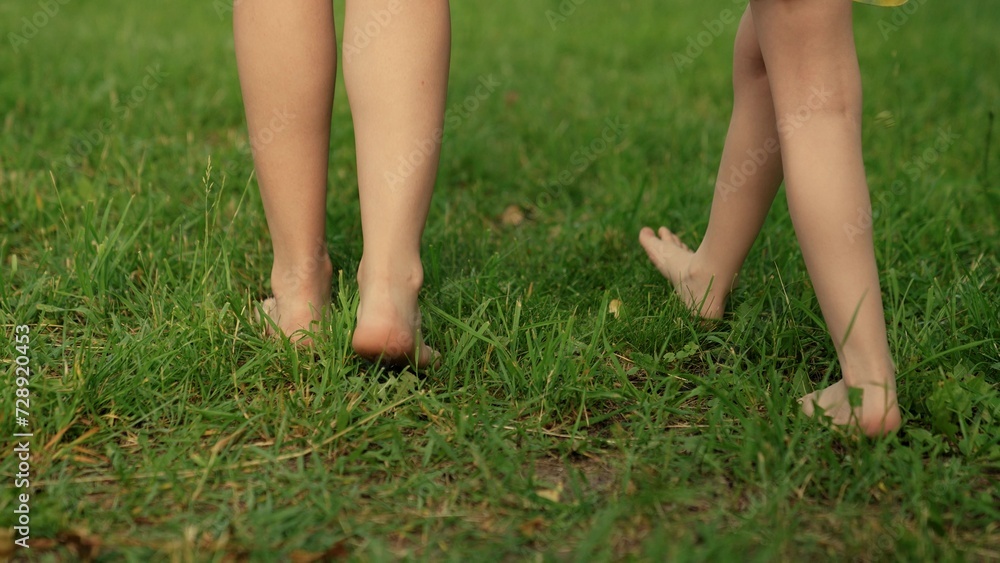 Family walk barefoot on green lawn on sunny day. Barefoot mom, boy, girl go on green grass in park. Bare feet mom, child, close-up go on green grass. Concept healthy lifestyle. Kid, mother fun outdoor