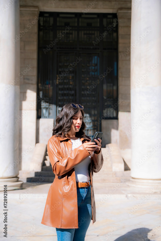 Happy young mexican woman taking selfie and top looking at screen of smartphone while sitting in front of blurred Bellas Fine Arts Palace in Mexico City and wearing fancy clothes
