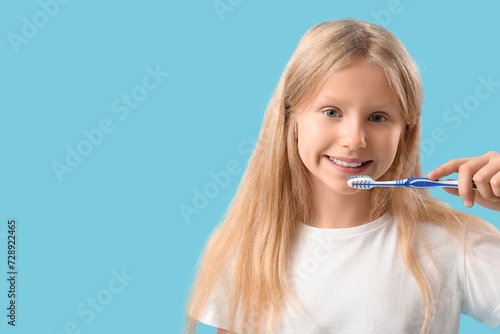 Happy little girl brushing her teeth on blue background