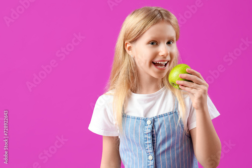Happy little girl with healthy teeth and fresh apple on purple background