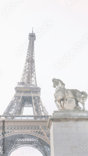 The Eiffel Tower and The statue of Pegasus, an equestrian statue called Mercure Monte sur Pegase, in soft foggy tone in Paris, France