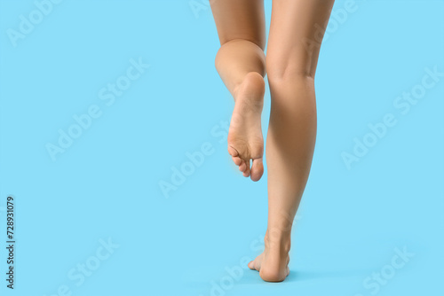 Barefoot woman walking on blue background, back view