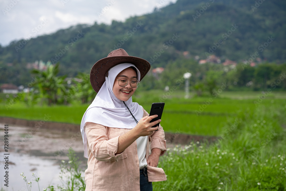 Fototapeta premium young woman farmer using mobile checking report of agriculture in farm. Rice field. technology agriculture koncept