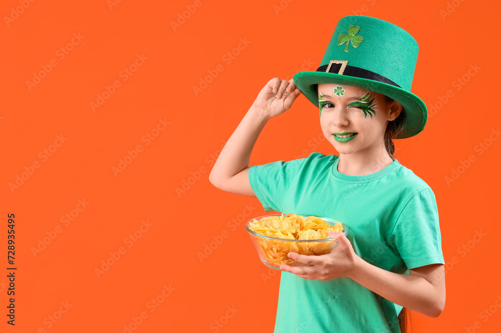 Funny girl with face painting, leprechaun's hat and potato chips on orange background. St. Patrick's Day celebration Funny girl with face painting, leprechaun's hat and potato chips on orange background. St. Patrick's Day celebration