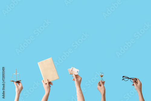 Female hands holding hourglass, scales of justice, book and money on blue background