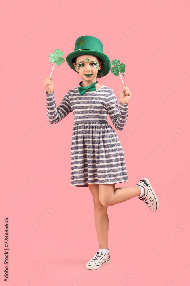 Funny girl with face painting, clovers and leprechaun's hat on pink background. St. Patrick's Day celebration Funny girl with face painting, clovers and leprechaun's hat on pink background. St. Patrick's Day celebration