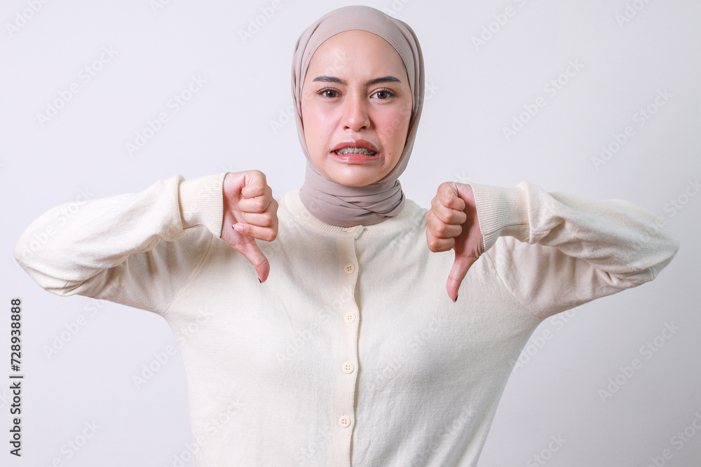 Young Asian muslim girl with braces and wearing hijab showing two thumbs down at camera. Negative emotions concept Young Asian muslim girl with braces and wearing hijab showing two thumbs down at camera. Negative emotions concept
