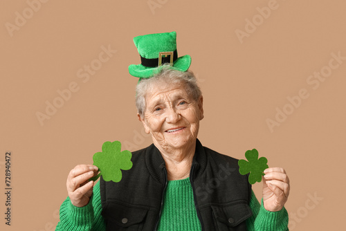 Senior woman in leprechaun hat with clover on brown background. St. Patrick's Day celebration