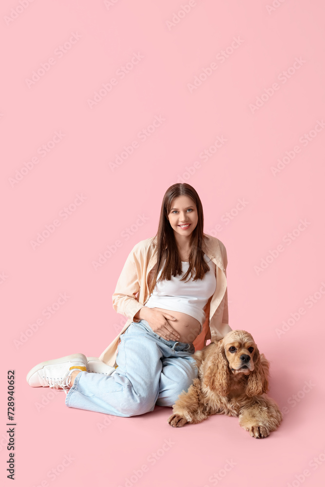 Young pregnant woman with cute cocker spaniel sitting on pink background Young pregnant woman with cute cocker spaniel sitting on pink background
