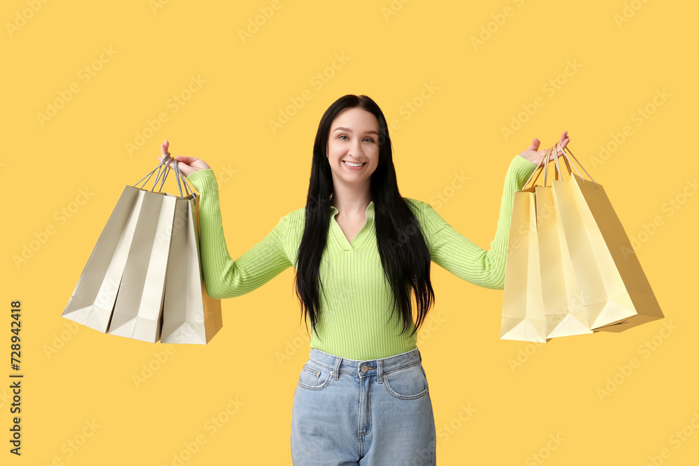 Beautiful young woman with shopping bags on yellow background. International Women's Day