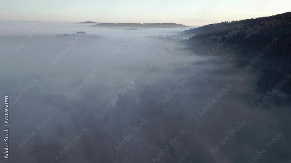 Aerial view of hilly, serene landscape of a forested area enveloped in mist during early morning. Aerial view of hilly, serene landscape of a forested area enveloped in mist during early morning.