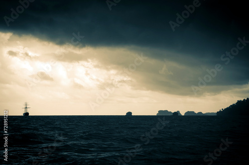 Classic sailing ship in the light of a huge storm with sunlight behind the clouds