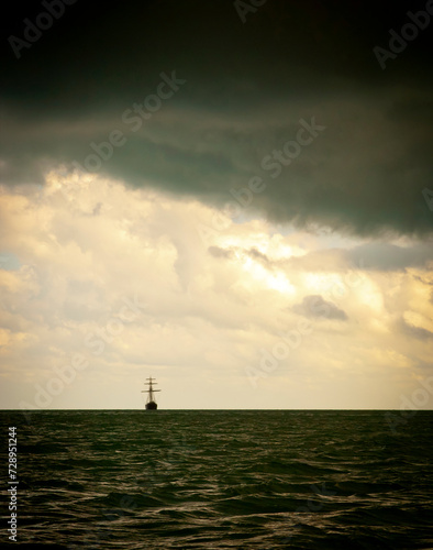 Classic sailing ship in the light of a huge storm with sunlight behind the clouds