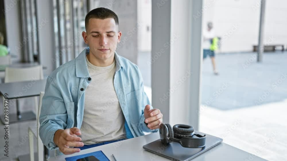 Young hispanic man using smartphone in a modern university library, with laptop and headphones on desk. Young hispanic man using smartphone in a modern university library, with laptop and headphones on desk.