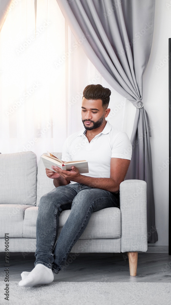 Home reading. Book relax. Handsome involved guy enjoying interesting novel studying information sitting comfortable sofa in light room interior.