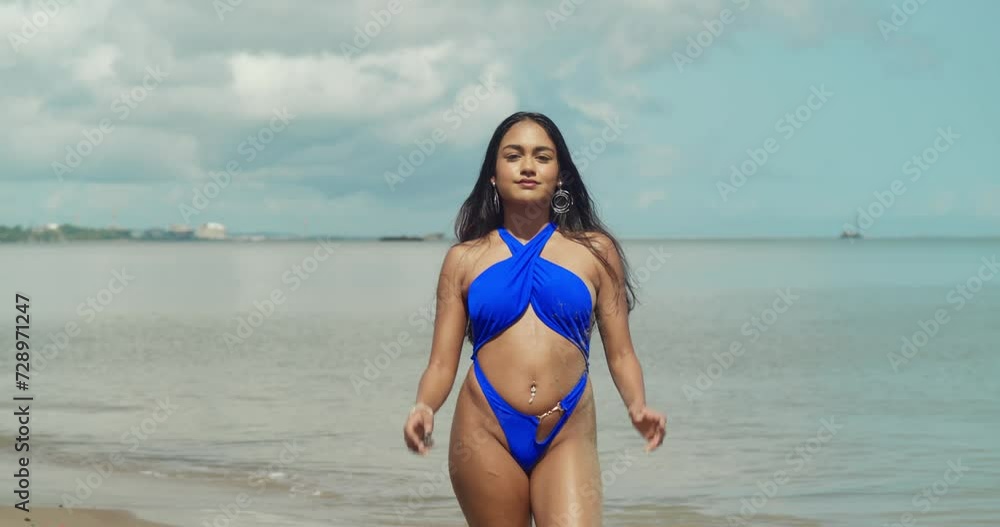 In a blue bikini, an Indian girl brings a vibrant presence to a sunny day in the Caribbean while walking in the sand In a blue bikini, an Indian girl brings a vibrant presence to a sunny day in the Caribbean while walking in the sand