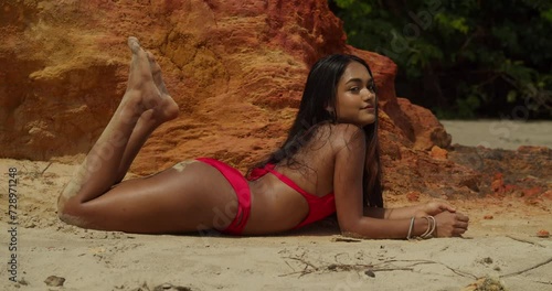 On a tropical beach in the Caribbean, an Indian girl showcases her beauty in a red bikini laying in the sand photo