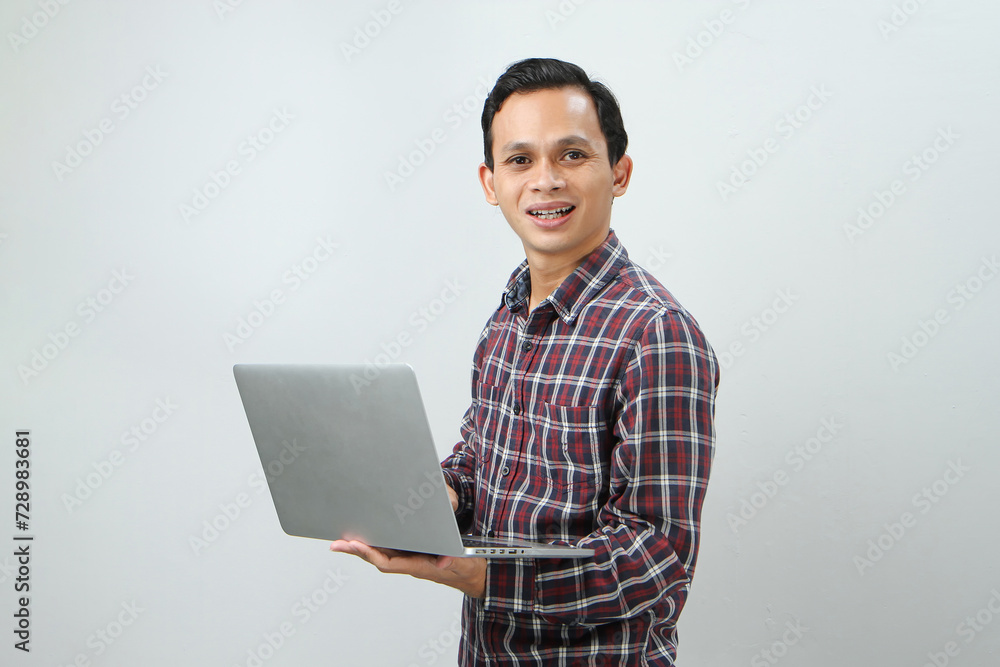 Happy asian indonesian man holding laptop computer on isolated background Happy asian indonesian man holding laptop computer on isolated background