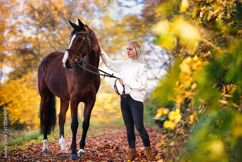 Young blonde girl with her horse walking through a colorful autumn forest. © RD-Fotografie