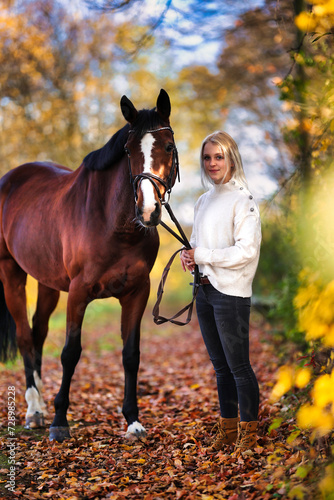 Young blonde girl with her horse walking through a colorful autumn forest.