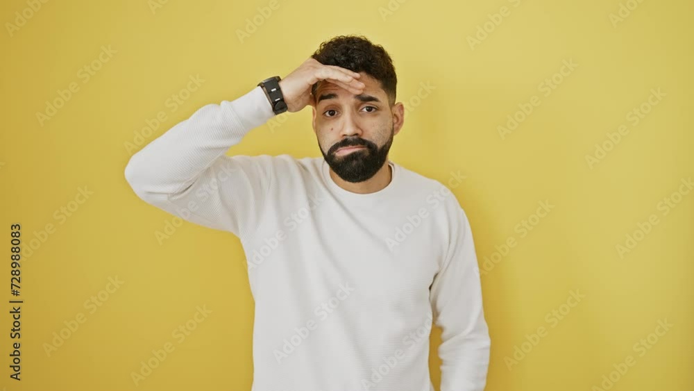 Stressed young man stands in trouble, worried about crisis problem, hand on his forehead against isolated yellow background Stressed young man stands in trouble, worried about crisis problem, hand on his forehead against isolated yellow background