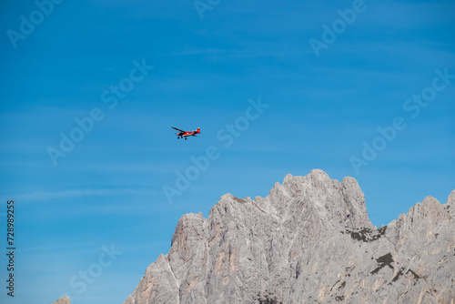 Small airplane flying over the majestic mountain ridges of Carnic Alps near Sauris di Sopra, Friuli Venezia Giulia, border Austria Italy. Serene tranquil atmosphere in Italian Alps. Transportation